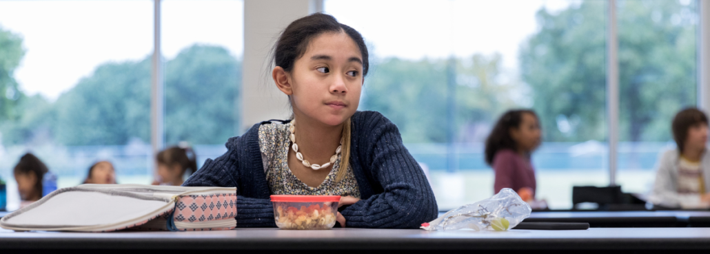 Girl sitting alone at lunch table in cafeteria